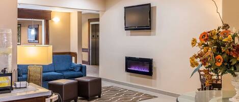 Un moderno vestíbulo de hotel con área de descanso, una recepción, una chimenea y un televisor montado en la pared.