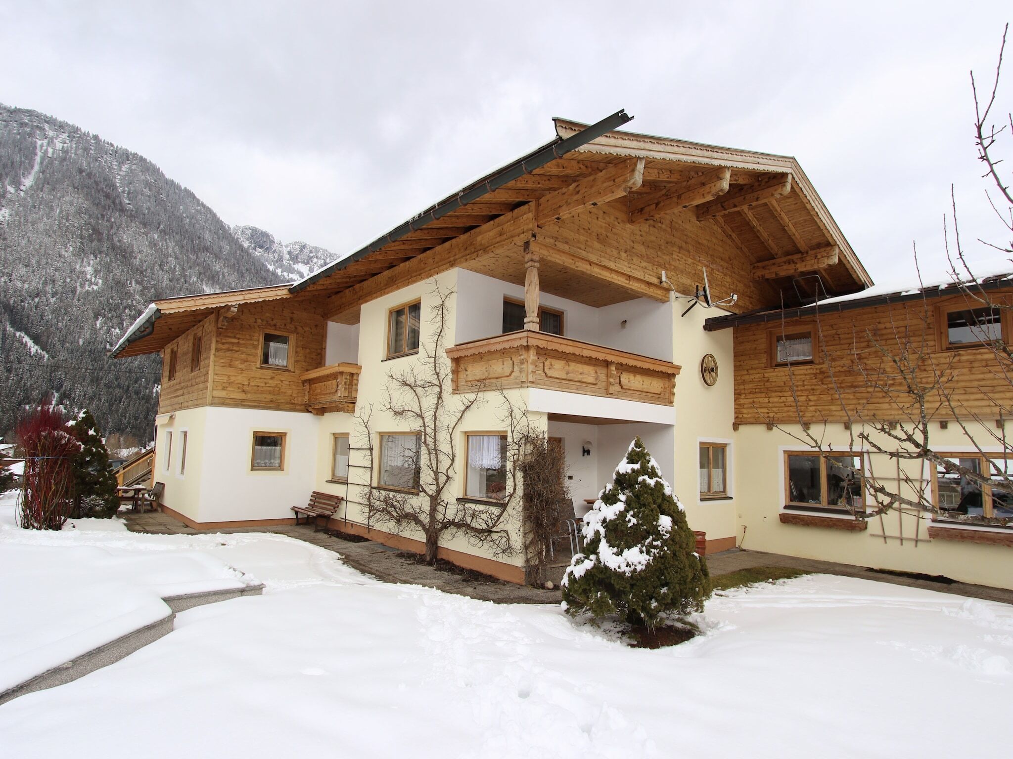 Une maison en bois à deux étages, dotée d’un balcon, entourée d’un paysage enneigé et de montagnes.