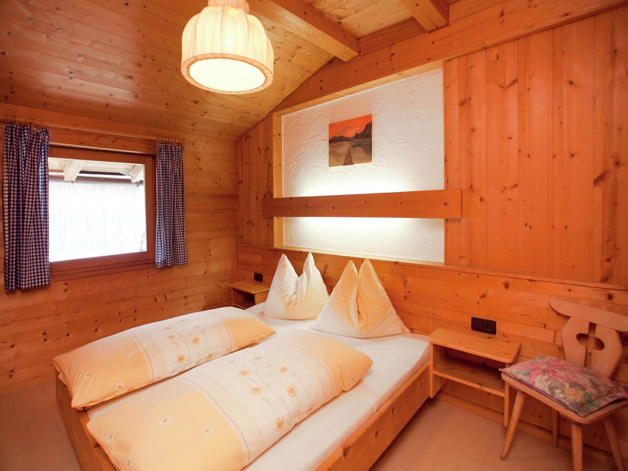 Una habitación de cabaña de madera con una cama, una mesita pequeña, una silla y una ventana con cortinas.