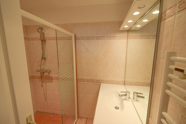 A bathroom with a glass shower enclosure, a white sink, and a towel rack.