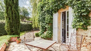 A stone patio with two metal chairs and a table, surrounded by greenery and a stone wall.