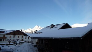 Ein mit Schnee bedeckter Berg mit blauem Himmel, ein Holzhaus mit verschneitem Dach und ein weißes Gebäude mit einem Schild.