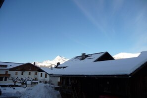 Ein mit Schnee bedeckter Berg mit blauem Himmel, ein Holzhaus mit verschneitem Dach und ein weißes Gebäude mit einem Schild.