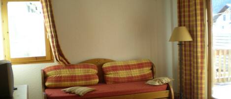Una habitación con un banco de madera con cojín rojo, una mesita y una lámpara.