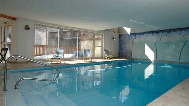 Ein Hallenbad mit klarem Wasser, Sprungbrett und Liegestühlen.
