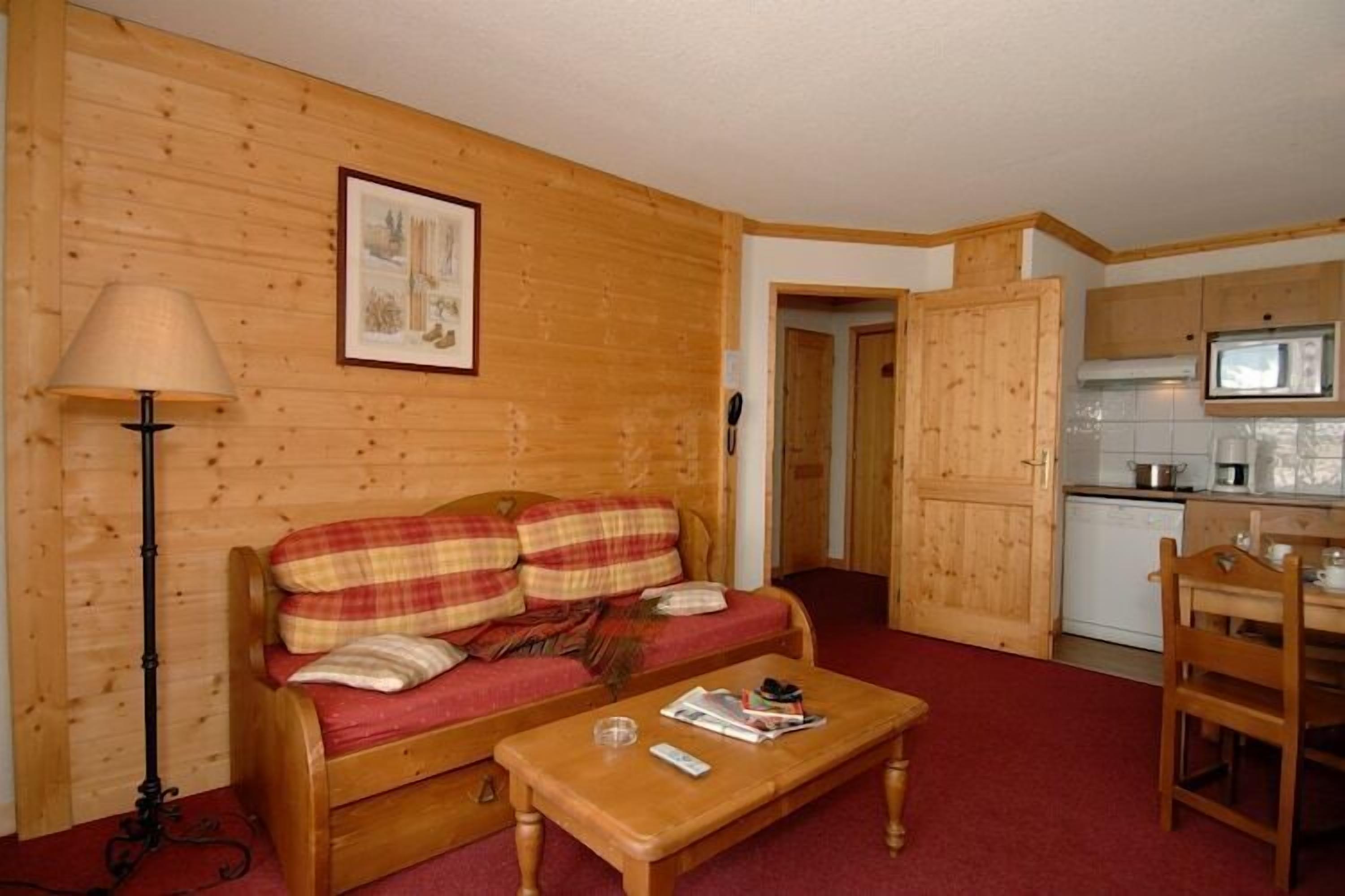 A cozy room with a wooden sofa, a small table, and a kitchen area with cabinets and a microwave.