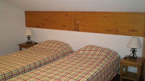 Ein Zimmer mit zwei Einzelbetten, jeweils mit einem hölzernen Kopfstück, sowie zwei Nachttischen mit Lampen.