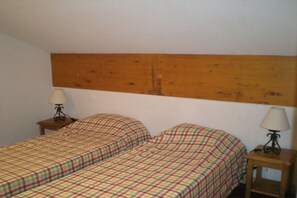 Ein Zimmer mit zwei Einzelbetten, jeweils mit einem hölzernen Kopfstück, sowie zwei Nachttischen mit Lampen.