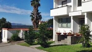 Un moderno edificio de dos pisos con un balcón, rodeado de vegetación y un cielo despejado.