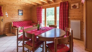A wooden cabin interior with a round dining table, red upholstered chairs, a bench, and a window with red curtains. - Chalet in La Bresse near Forest & Lake (La Bresse)
