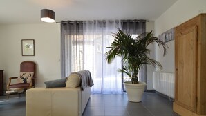A living room with a sofa, a chair with a deer cushion, a large potted plant, a wooden cabinet, and a window with sheer curtains. - Holiday Home near Opal Coast Wierre-Effroy (Wierre-Effroy (Londefort))