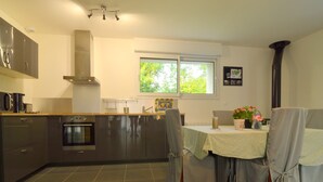 A modern kitchen with a built-in oven, a microwave, and a stainless steel range hood. There is a dining area with a table and chairs, and a window providing natural light. - Holiday Home near Opal Coast Wierre-Effroy (Wierre-Effroy (Londefort))