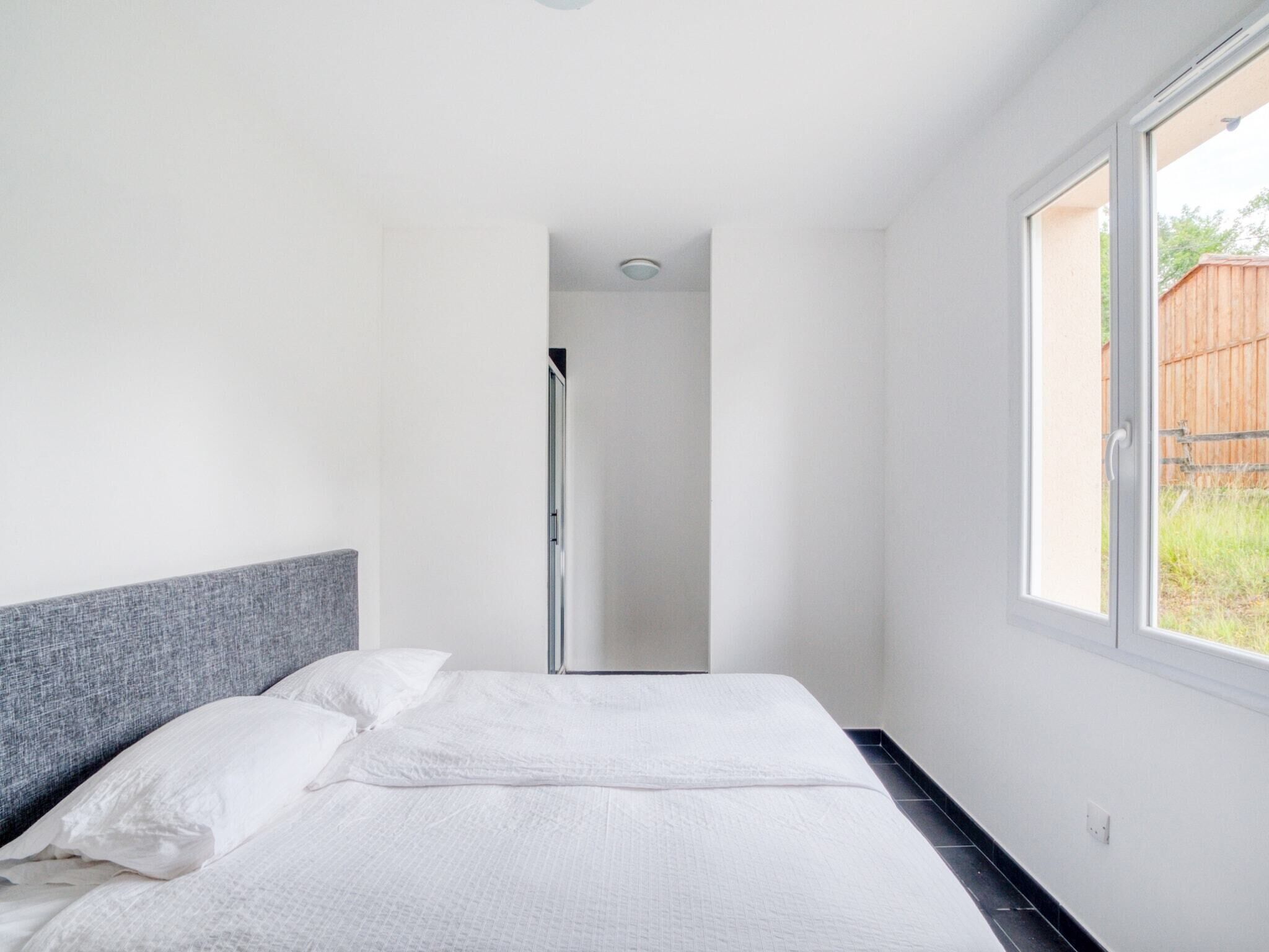 A bedroom with a bed, a grey headboard, a large window, and a door leading to a bathroom.