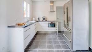 Een moderne keuken met witte kasten, een roestvrijstalen koelkast, een inbouwoven en een raam dat natuurlijk licht biedt.