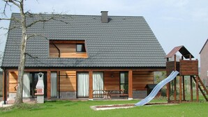 Una casa moderna con techo inclinado, terraza de madera y tobogán.