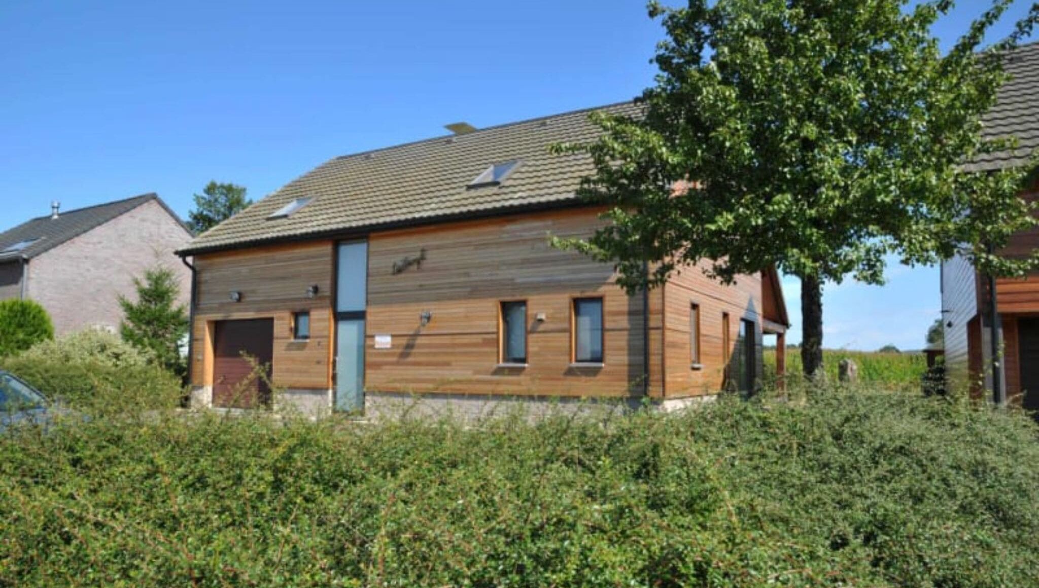 A modern two-story house with a sloped roof, large windows, and a visible chimney.