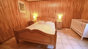 Una habitación con paneles de madera, una cama, mesitas de noche y una cuna.
