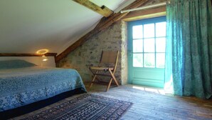 Un dormitorio con techo inclinado, cama con ropa de cama estampada, una silla y una ventana con cortinas.