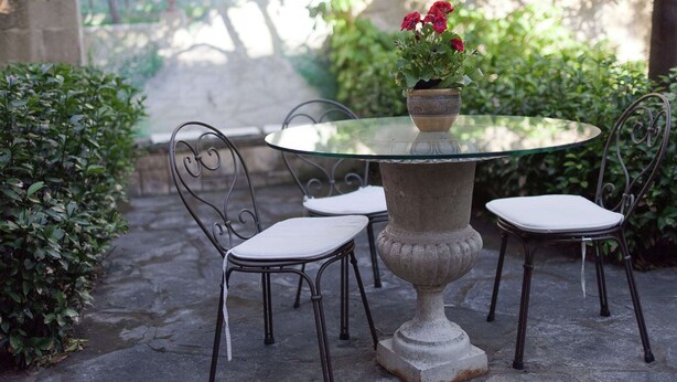 A round glass table with a stone pedestal base, surrounded by four metal chairs with white cushions.
