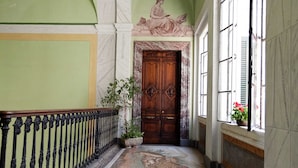 A hallway with a marble floor, a wooden door, and a window with flowers.