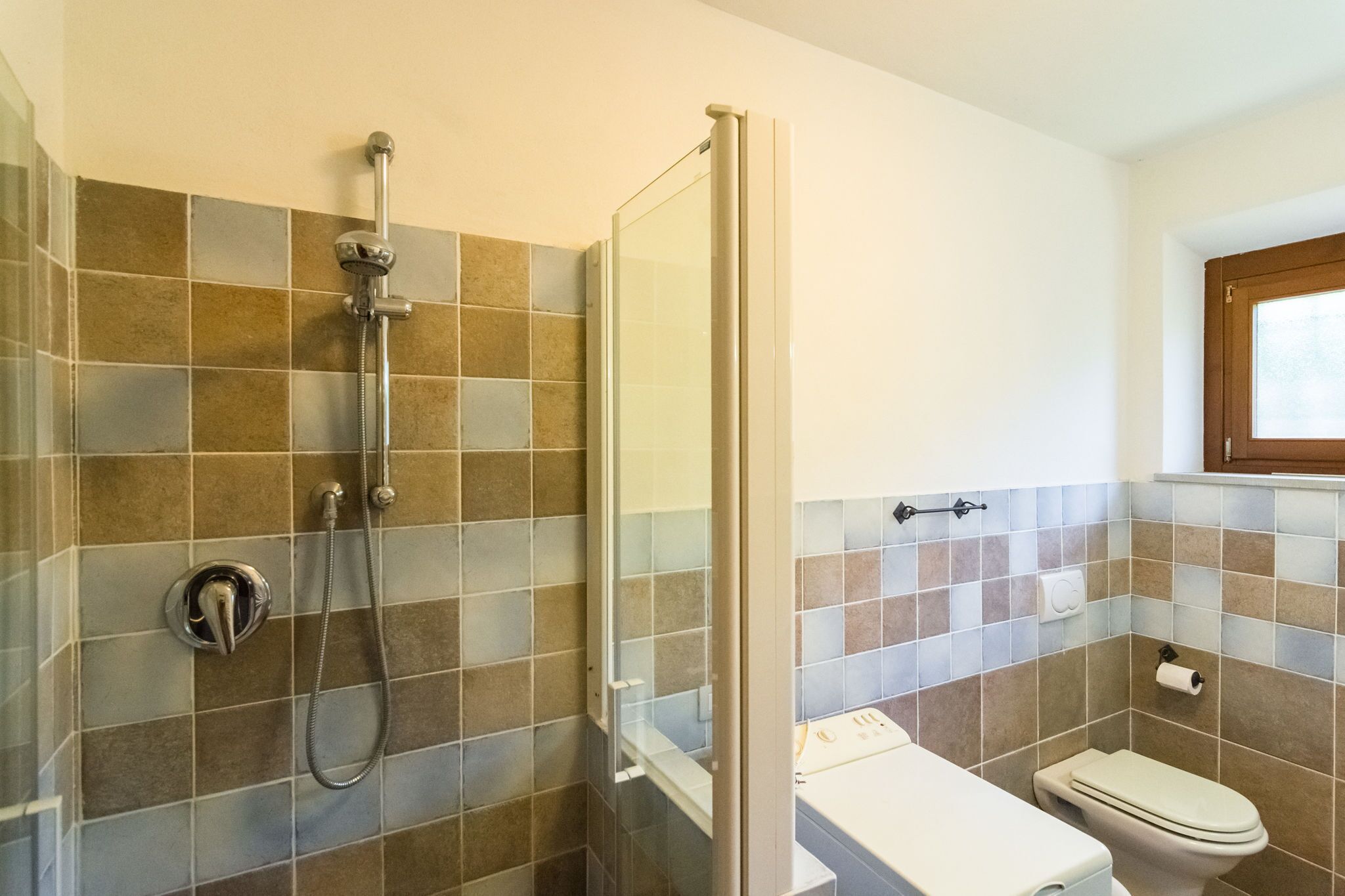 Une salle de bain avec une douche, des toilettes et une fenêtre.