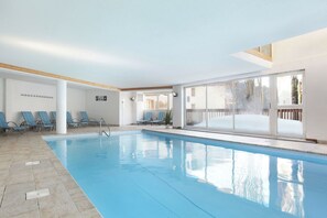 Una piscina interior con sillas de descanso y vistas al exterior.