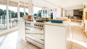 A modern kitchen with a central island, large windows, and a dining area with a table and chairs.