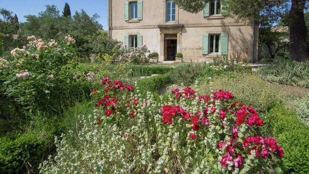 Edifici de dues plantes amb una entrada central, envoltat de jardins exuberants i plantes florentes.