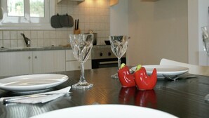 A dining table with plates, cutlery, and wine glasses, set in a kitchen with white cabinets and a window.