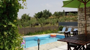 A pool area with a stone wall, lounge chairs, and a pergola with a green umbrella.