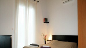 A hotel room with a bed, a bedside table with a lamp, a bookshelf, and a window with curtains.