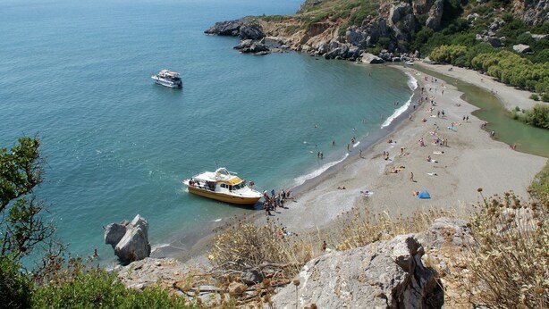 A coastal beach with a boat docked near the shore, rocky cliffs, and a clear view of the sea.