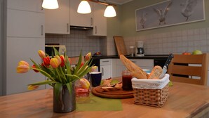 Una cucina con mobili bianchi, un tavolo di legno con un vaso di tulipani, un cesto di pane e un quadro appeso al muro.