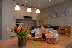 Enjoy meals in this kitchen with a dining table, vase, jar of jam, and bread basket.