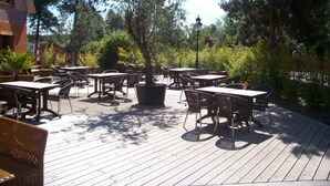 An outdoor patio with multiple tables and chairs, surrounded by trees and greenery.