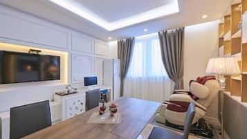 Une chambre d’hôtel moderne dotée d’un coin repas, d’un fauteuil massant, d’un téléviseur à écran plat et d’un bureau avec un ordinateur.