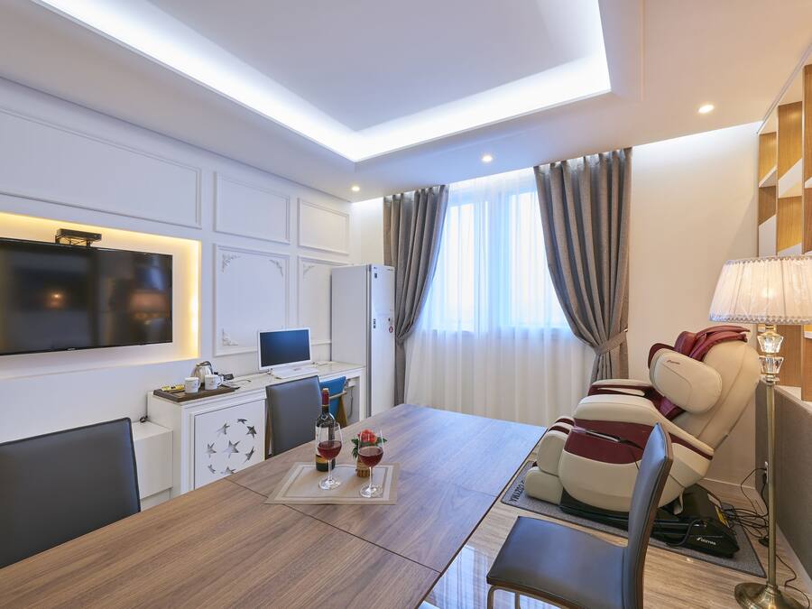 Une chambre d’hôtel moderne dotée d’un coin repas, d’un fauteuil massant, d’un téléviseur à écran plat et d’un bureau avec un ordinateur.