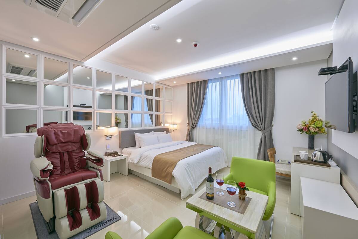 Una habitación de hotel moderna con cama, sillón de masaje, zona de comedor y televisión.