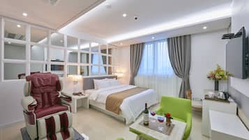 A modern hotel room with a bed, a massage chair, a dining area, and a TV.