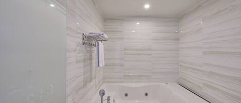 A modern bathroom with a large bathtub, marble walls, and a glass shower enclosure.