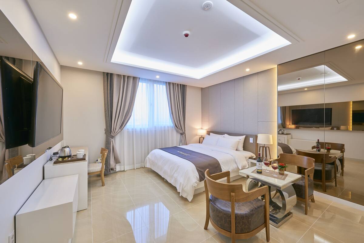 Una habitación de hotel moderna con una cama grande, un escritorio, una silla, una mesa de comedor y un televisor.