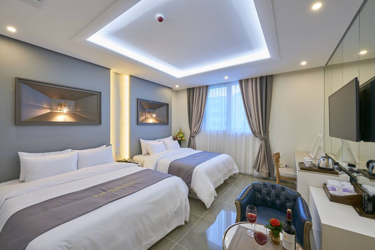 Habitación de hotel con dos camas, un escritorio, una silla, un televisor y una lámpara en el techo.