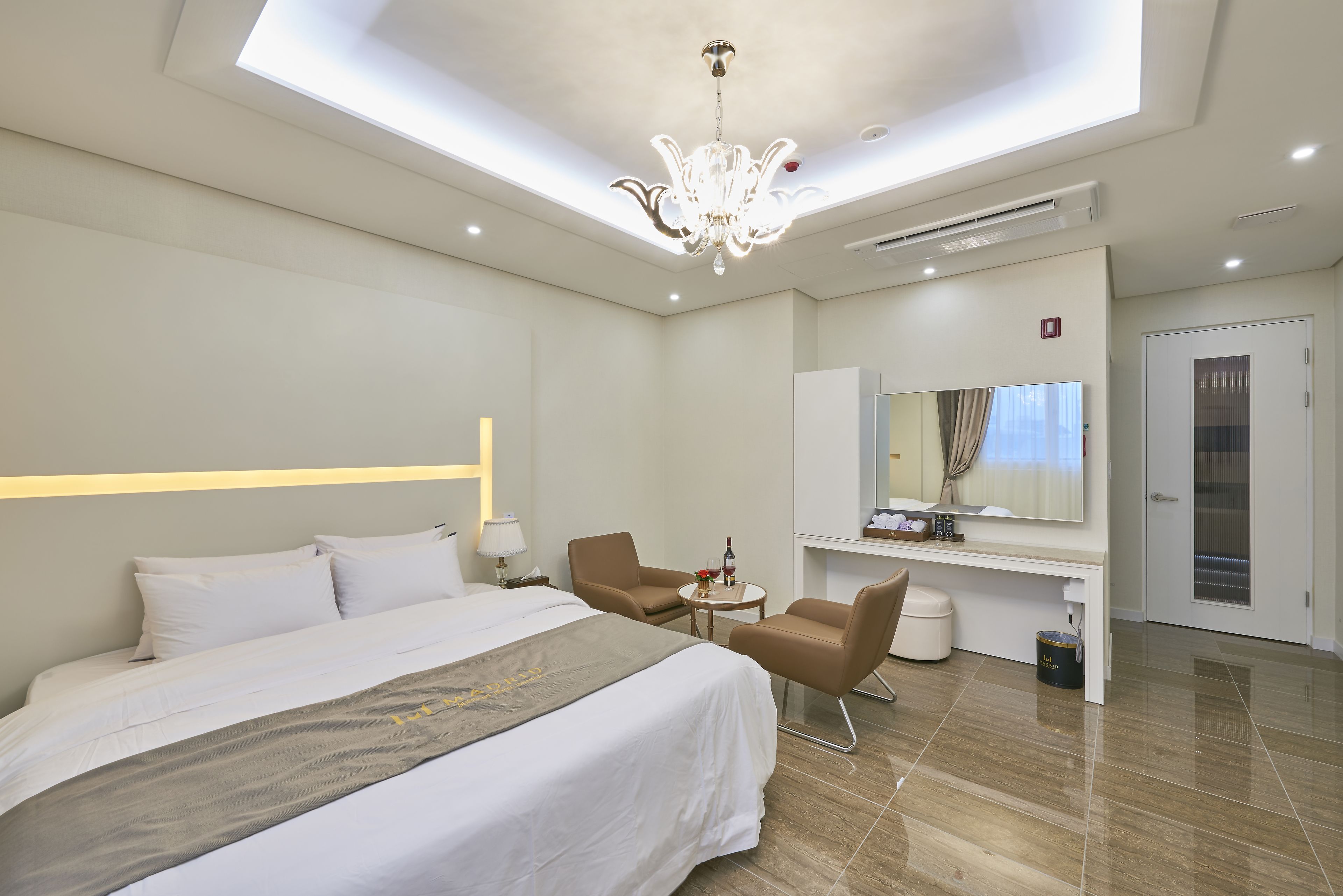 A modern hotel room with a large bed, two chairs, a desk, and a mirror.