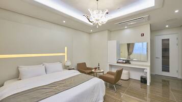 A modern hotel room with a large bed, two chairs, a desk, and a mirror.