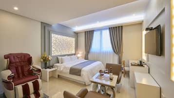 A modern hotel room with a bed, massage chair, dining table, and a TV.