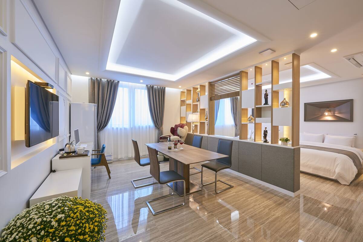 Una habitación de hotel moderna con zona de comedor, sofá, televisor y cama.