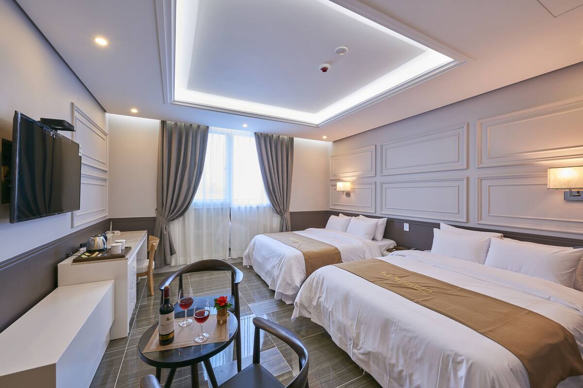 Habitación de hotel con dos camas, un escritorio, una silla, un televisor y una ventana con cortinas.