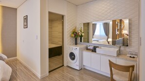 A hotel room with a washing machine, a vanity with a mirror, a wooden chair, and a bed. - Madrid Hotel Gwangju (Gwangju)