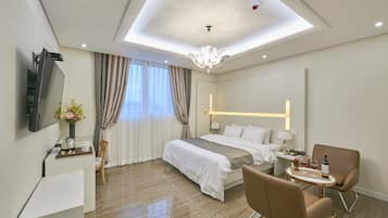 A modern hotel room with a bed, a desk, a chair, a TV, and a chandelier.