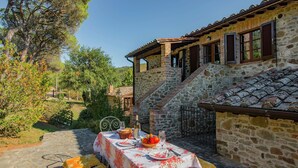 A stone building with a dining table set outdoors, surrounded by greenery. - Scenic Farmhouse with Pool (Città Della Pieve)